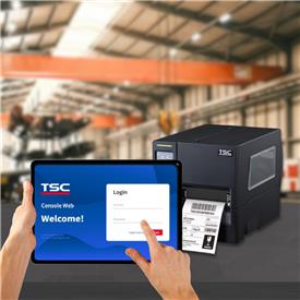 A hand holding a tablet displaying the TSC Web Console sign-in page. In the background, a TSC label printer sits in an industrial setting.