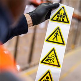 A warehouse worker holds up a roll of hazard warning labels.